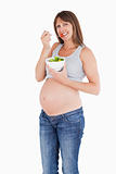 Attractive pregnant woman eating a cherry tomato while holding a