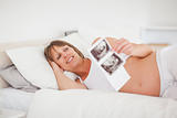 Pretty pregnant woman holding an ultrasound scan while lying on 