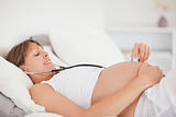 Cute pregnant woman using a stethoscope while lying on a bed