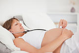Beautiful pregnant woman using a stethoscope while lying on a be