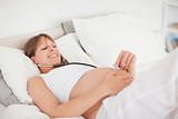 Good looking pregnant woman using a stethoscope while lying on a