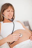 Attractive pregnant woman using a stethoscope while lying on a bed