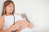 Beautiful pregnant woman using a stethoscope while lying on a bed