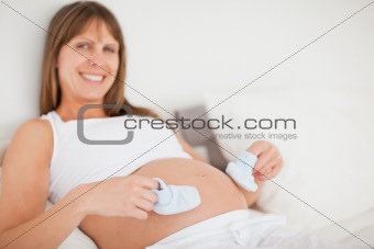 Attractive pregnant woman playing with little socks while lying 