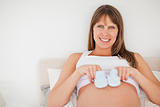 Cute pregnant woman playing with little socks while lying on a b