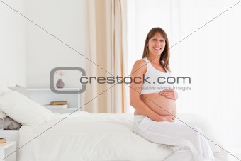 Beautiful pregnant female posing while sitting on a bed