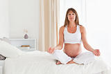 Good looking pregnant female doing yoga on a bed