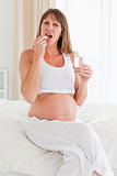 Beautiful pregnant female taking a pill while sitting on a bed