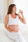 Charming pregnant female taking a pill while sitting on a bed