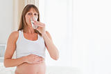 Cute pregnant female taking a pill while sitting on a bed