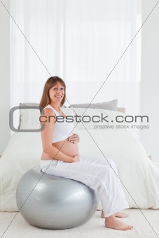 Beautiful pregnant female caressing her belly while sitting on a
