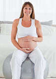 Charming pregnant female caressing her belly while sitting on a 