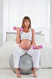 Beautiful pregnant female using a dumbbell while sitting