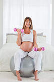 Attractive pregnant female using a dumbbell while sitting on a gym ball(