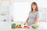 Beautiful pregnant woman posing while cooking vegetables