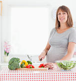 Good looking pregnant woman posing while cooking vegetables