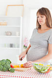 Charming pregnant woman posing while cooking vegetables