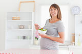 Lovely pregnant woman eating a cherry tomato while standing