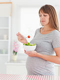 Good looking pregnant woman eating a cherry tomato while standing