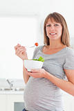 Pretty pregnant woman eating a cherry tomato while standing