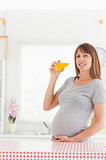 Pretty pregnant woman drinking a glass of orange juice while sta