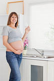 Pretty pregnant woman drinking a glass of water while standing