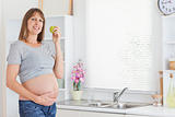 Pretty pregnant woman posing while holding a green apple