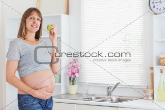 Pretty pregnant woman posing while holding a green apple
