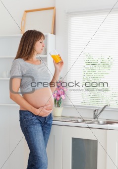 Attractive pregnant woman drinking a glass of orange juice while