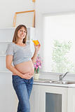 Beautiful pregnant woman holding a glass of orange juice while s