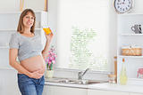 Attractive pregnant woman holding a glass of orange juice while 