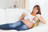 Attractive pregnant woman playing with baby shoes while lying