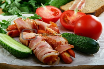 Sausages wrapped in bacon with vegetables and herbs.