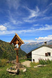 Wooden cross near rural house in Alps.