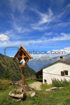 Wooden cross near rural house in Alps.