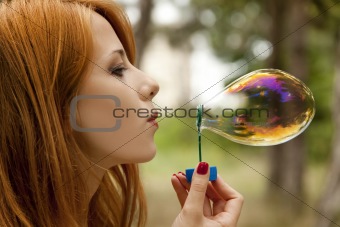 Redhead girl inflate soap bubble.