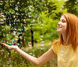 Redhead girl in the park under soap bubble rain.