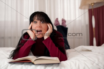 Beautiful young woman reading book in bedroom