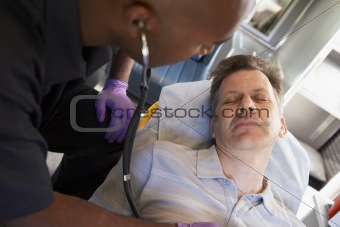 Paramedic using stethoscope on patient in ambulance