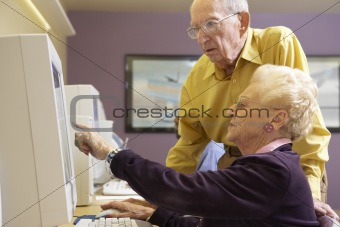 Senior man helping senior woman to use computer