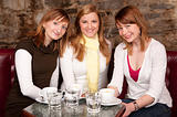 Three beautiful young students waiting drinking  coffee and having a debate in coffee shop