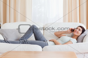 Young brunette calling while lying on a sofa