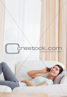 Portrait of a brunette calling while lying on a sofa