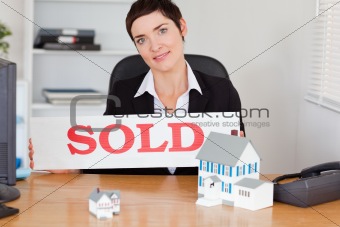 Female real estate agent with a sold panel and houses miniatures