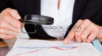 Female hands holding a magnifying glass above a chart in an office