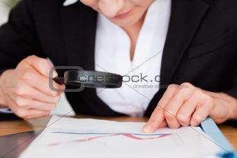 Feminine hands holding a magnifying glass above a chart