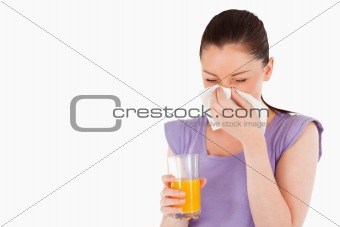 Good looking woman holding a glass of orange juice and sneezing 