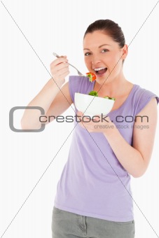 Good looking woman eating a bowl of salad while standing