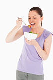 Beautiful woman eating a bowl of salad while standing