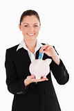 Charming woman in suit inserting a money bill in a pink piggy ba